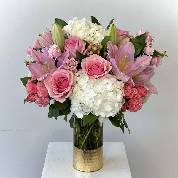 Pink roses and lilies arranged with white hydrangeas in a glass vase.