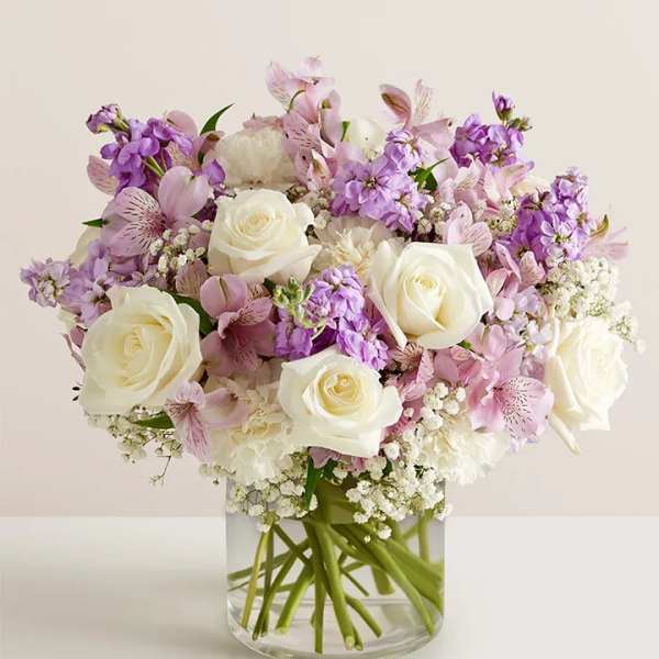 White roses and pink-purple flowers arranged in a clear glass vase