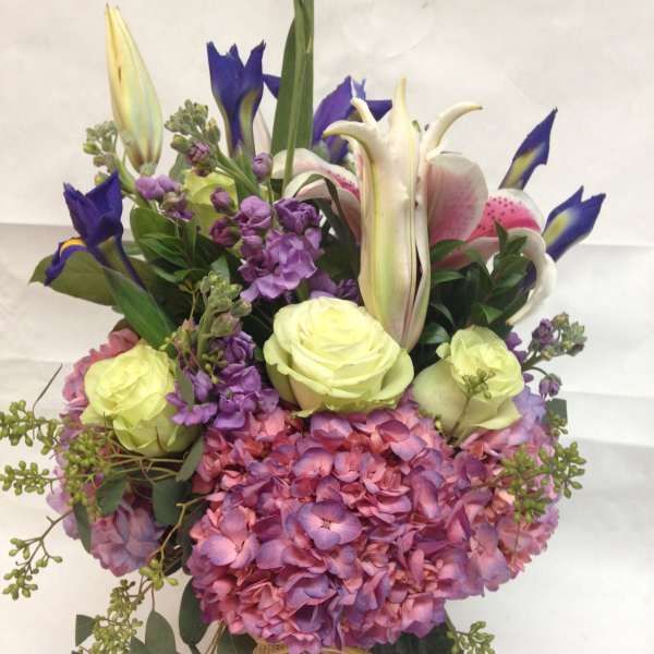 Bouquet of pink hydrangeas, lilies, irises, and pale roses in a burlap-wrapped vase