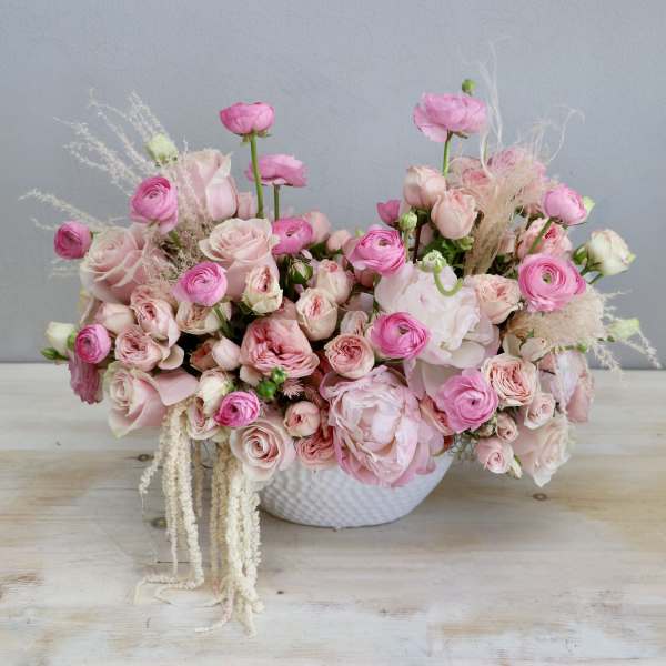 Low bowl arrangement of pink roses, ranunculus, and peonies in a white ceramic container