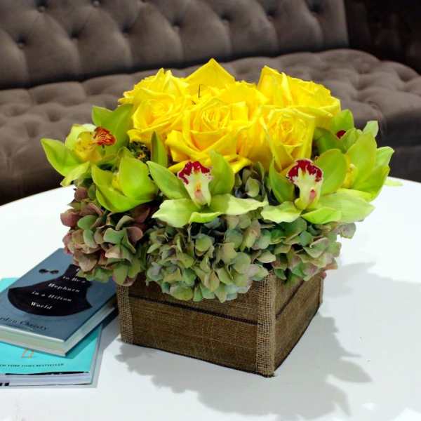 Yellow roses and green orchids in a square burlap-covered box