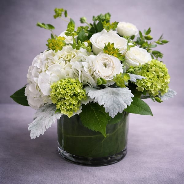 White floral arrangement in a glass vase with green accents