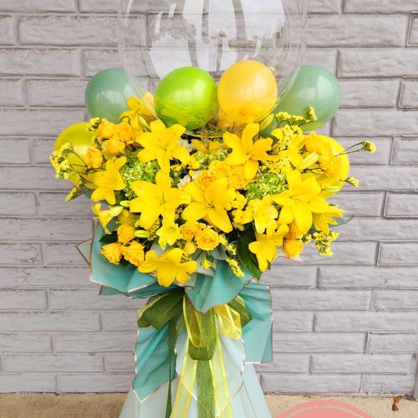 Yellow floral arrangement with balloons and a clear balloon topper