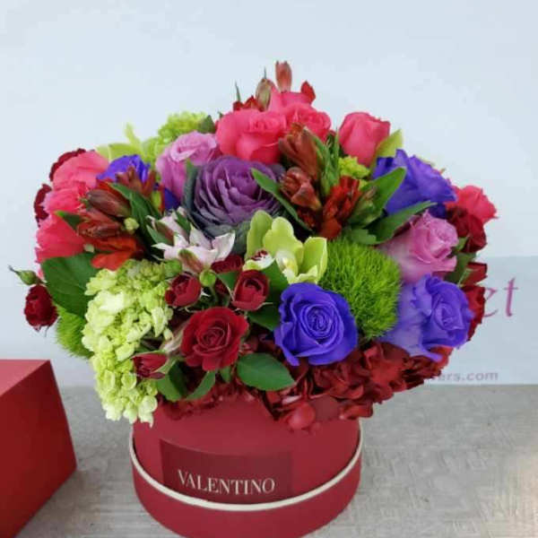 Colorful bouquet of roses and mixed flowers in a red round box