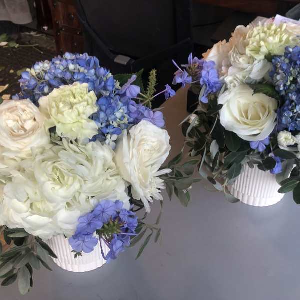 Two white and blue floral arrangements in ribbed white containers