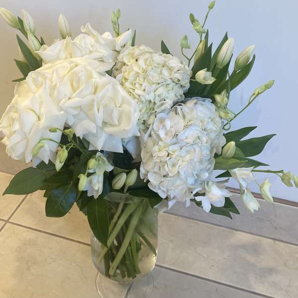 White hydrangea and lily bouquet in a clear glass vase