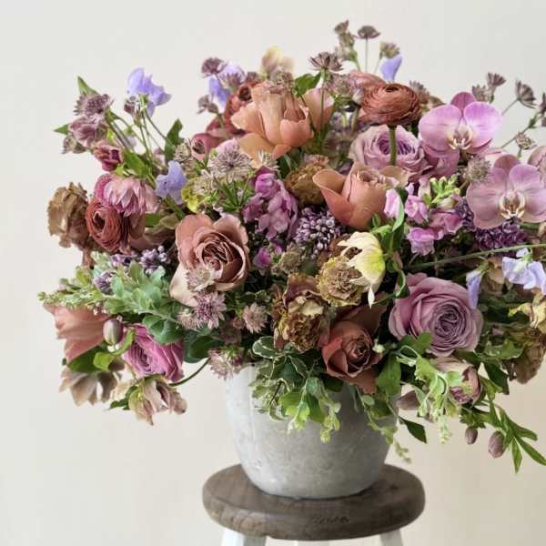 A mixed bouquet of pink, lavender, and peach flowers in a gray vase.