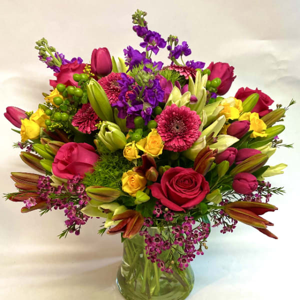 Mixed bouquet of pink, purple, and yellow flowers in a glass vase
