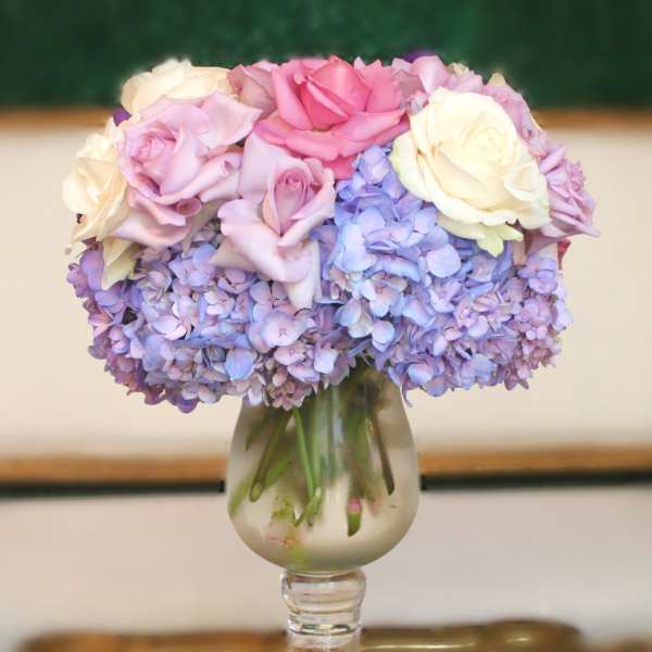 Pink and white roses arranged with lavender hydrangeas in a glass vase