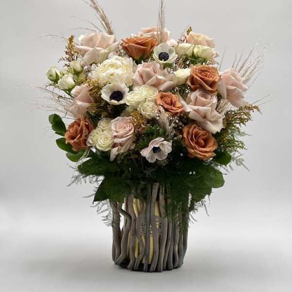 Bouquet of blush and peach roses with white accent flowers in a tall vase