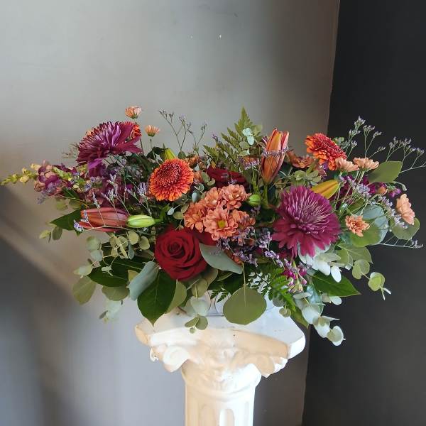 Mixed bouquet of roses, chrysanthemums, and lilies in a white vase