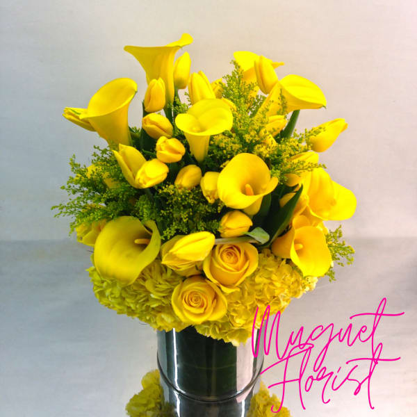 Yellow calla lilies and roses arranged in a silver vase