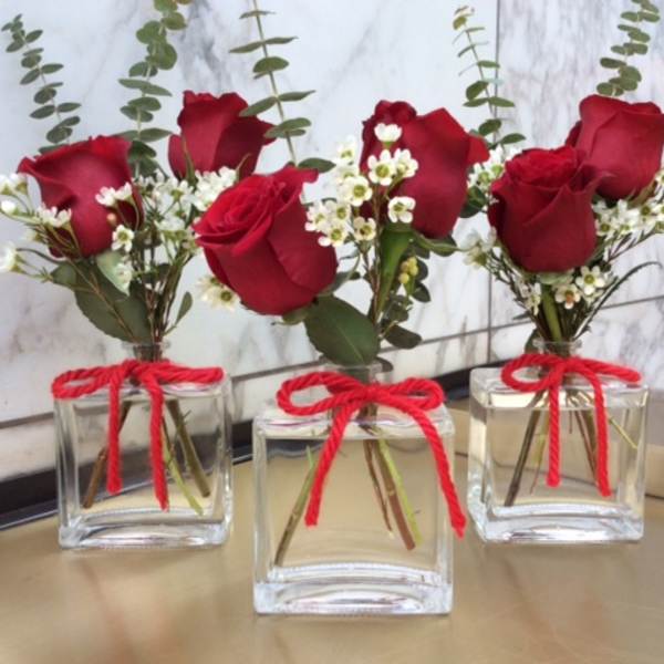 Three small rose arrangements in square glass vases with red bows