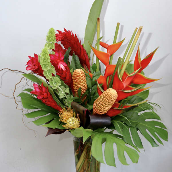 Tropical bouquet with red and orange flowers in a tall glass vase