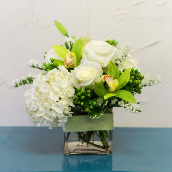 White roses and hydrangeas in a square glass vase with green accents
