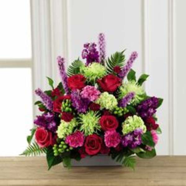 Mixed bouquet of red roses, purple flowers, and green accents in a low container