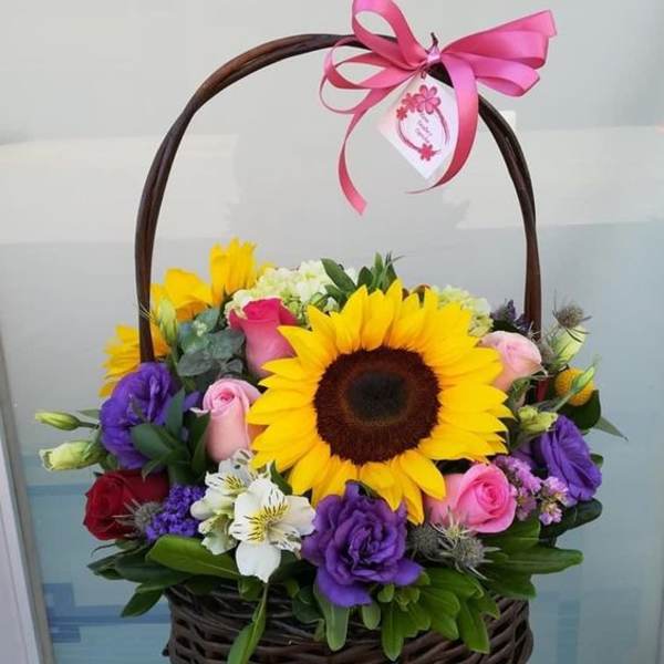 Basket of mixed flowers with a large sunflower and pink ribbon