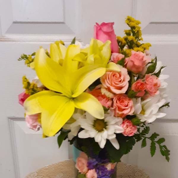 Bouquet of yellow lilies, pink roses, and white daisies in a glass vase