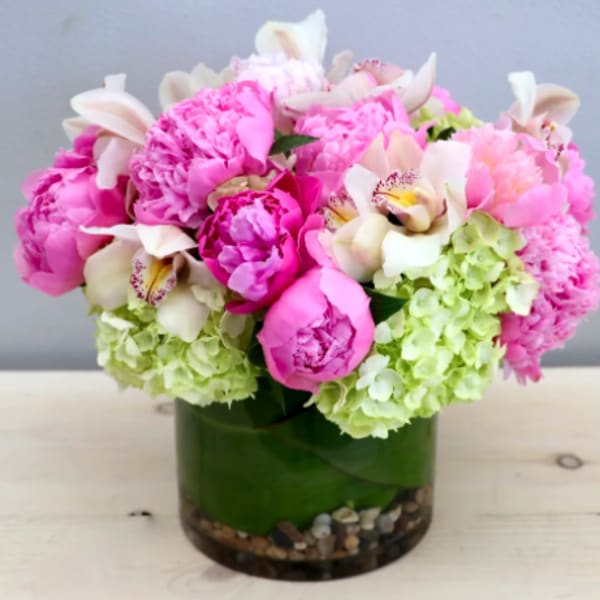 Compact arrangement of pink peonies, white orchids, and green hydrangeas in a glass vase