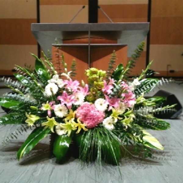 Large stage arrangement of pink lilies, white flowers, and lush greenery in front of a podium