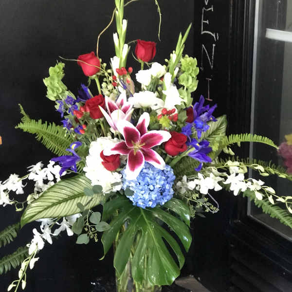 Tall mixed bouquet with red roses, lilies, and blue hydrangea in a glass vase