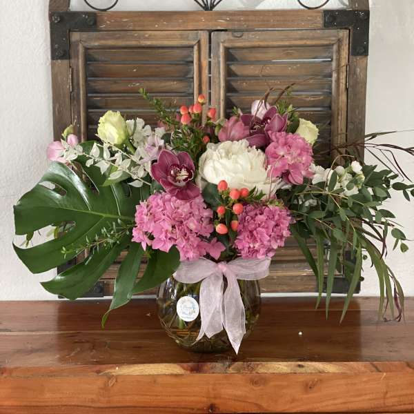 Pink and white floral arrangement in a glass vase with a ribbon
