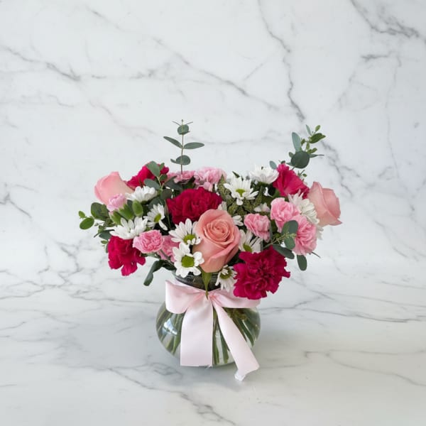 Pink and white mixed flower arrangement in a glass vase with a ribbon
