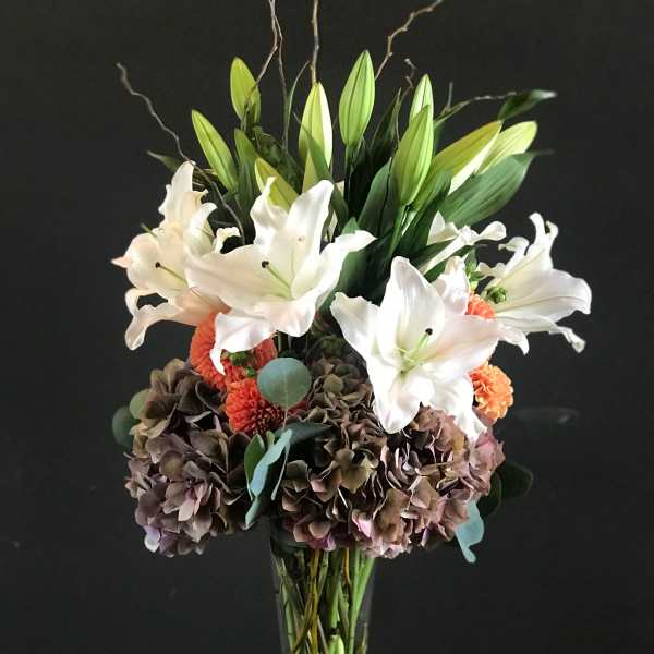 Tall bouquet of white lilies and hydrangeas in a clear glass vase