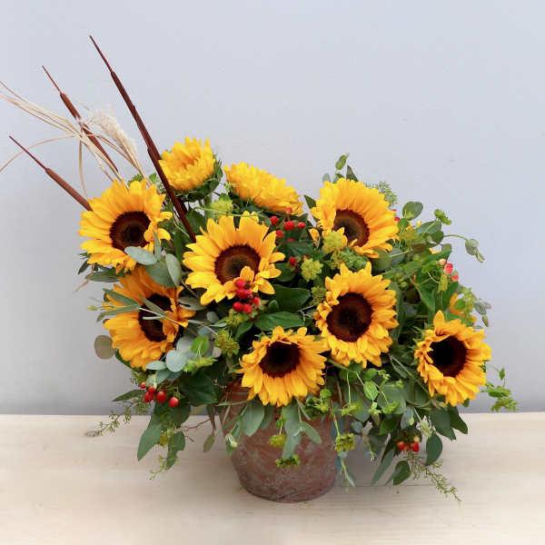 Asymmetrical arrangement of yellow sunflowers with red berries in a rustic pot