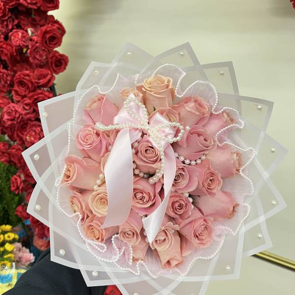 Pink rose bouquet wrapped in sheer paper with a satin ribbon and pearl accents