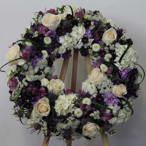 Floral wreath with white roses and purple flowers on an easel