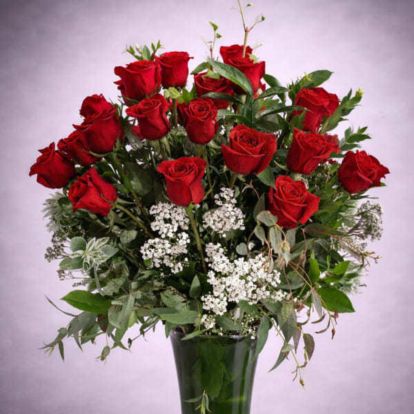Red roses arranged in a tall glass vase with white filler flowers