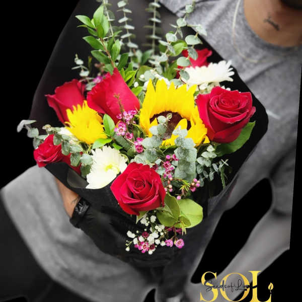 Bouquet of red roses, sunflowers, and white daisies wrapped in black paper