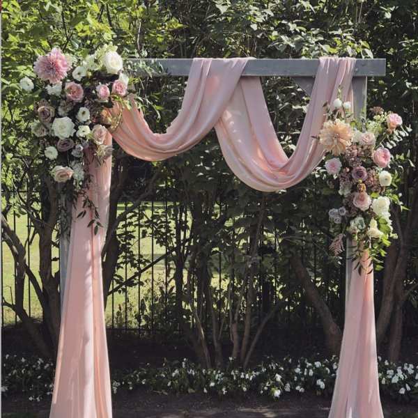 Pink draped wedding arch with pastel floral arrangements
