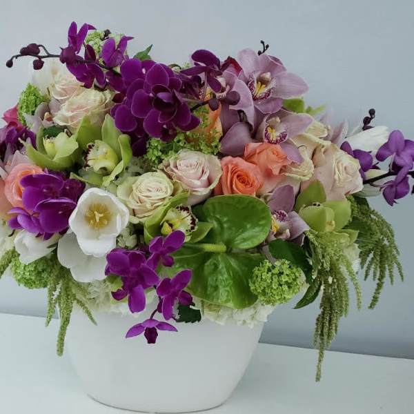 Mixed bouquet of purple orchids, roses, and white blooms in a white vase
