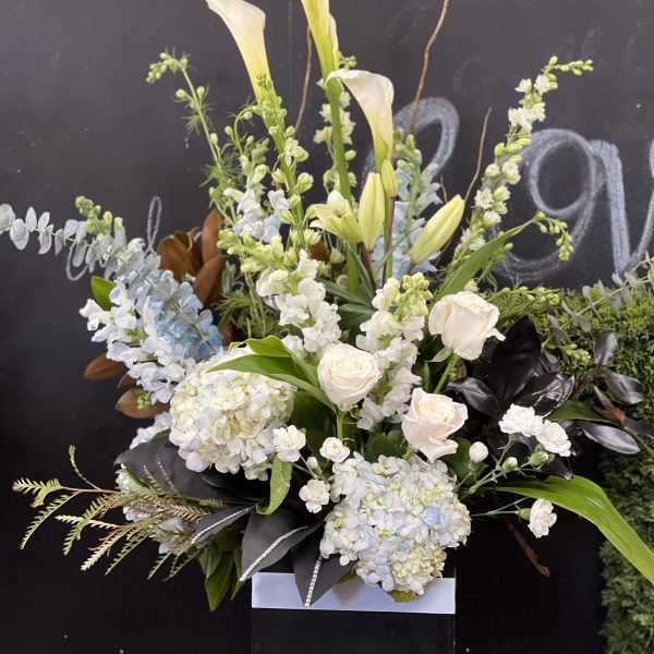 Tall white floral arrangement with lilies, roses, and hydrangeas in a black box