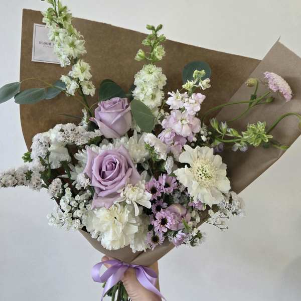 Hand-tied bouquet of lavender roses and white flowers wrapped in brown paper