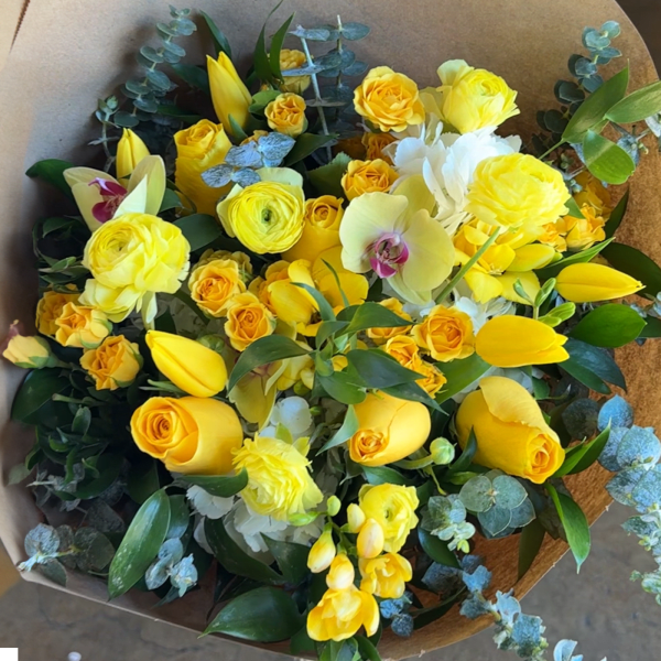 Yellow and white mixed bouquet with orchids and tulips wrapped in brown paper