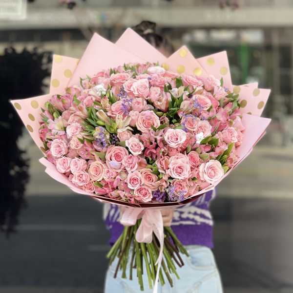 Large bouquet of pink roses and mixed blooms wrapped in pink paper with gold dots