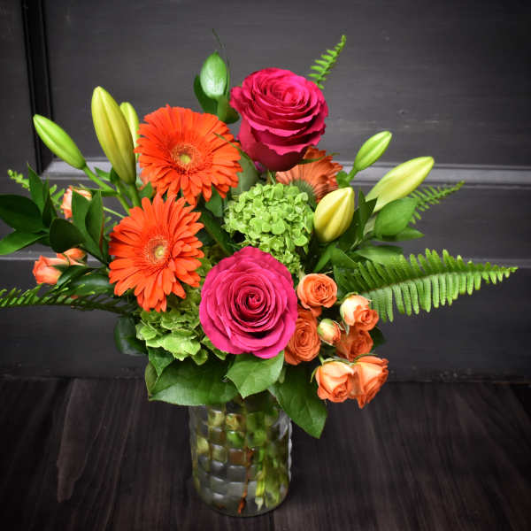 Bright mixed bouquet with pink roses, orange gerberas, and lilies in a glass vase
