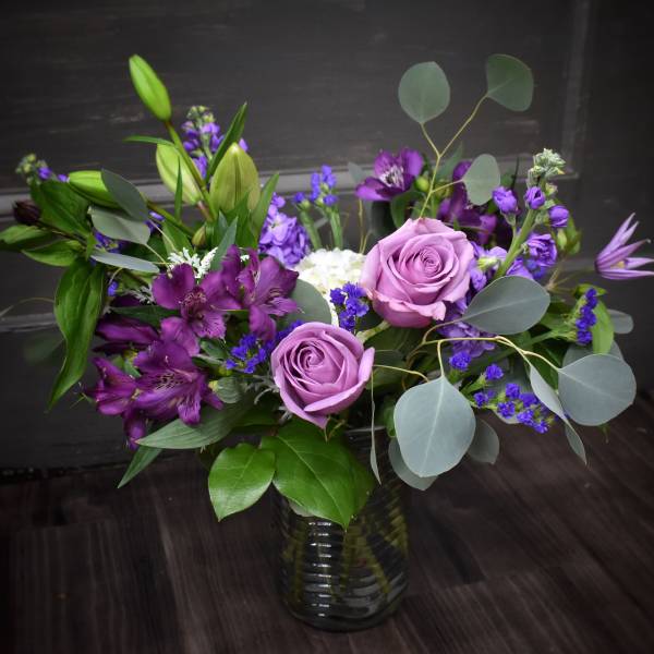 Purple roses and mixed purple flowers in a glass vase