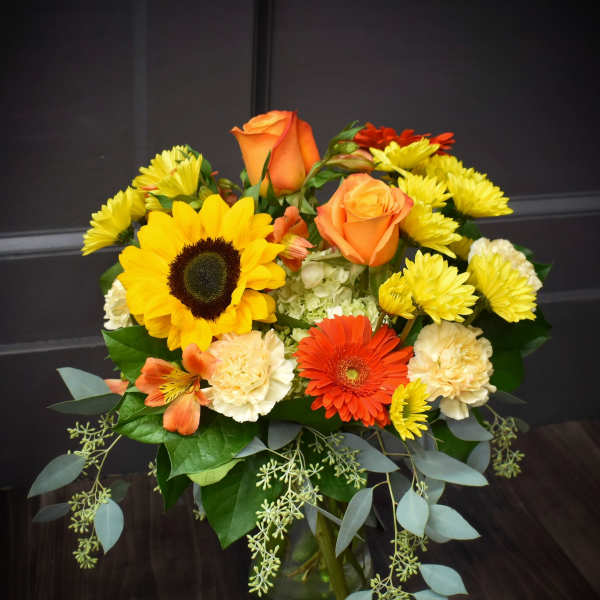 Mixed bouquet with sunflowers, orange roses, gerbera daisies, and yellow mums in a glass vase