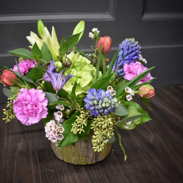 Mixed bouquet with pink carnations, lilies, and blue hyacinths in a rustic container