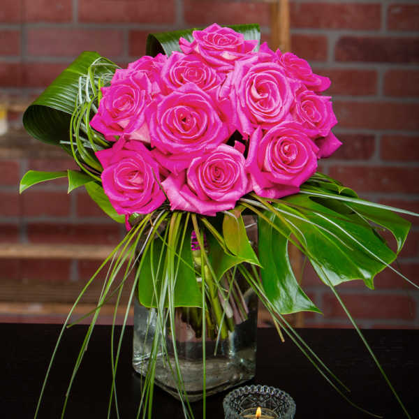 Hot pink roses arranged in a clear glass vase with tropical leaves
