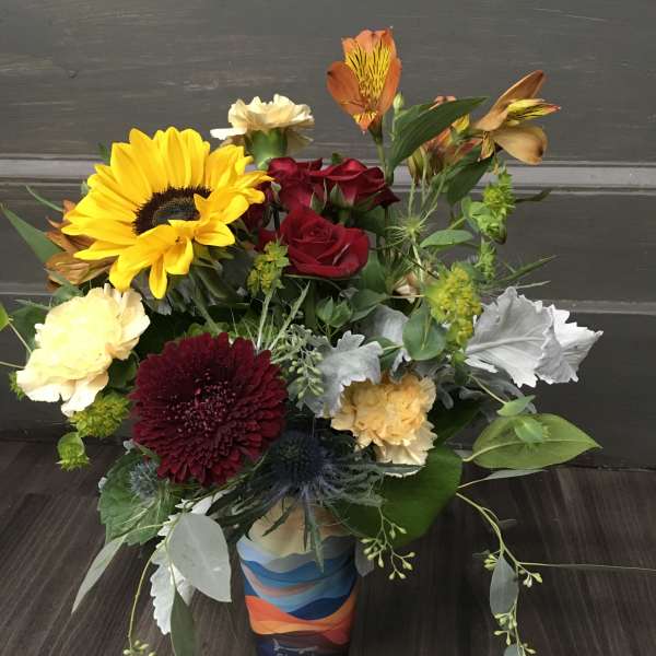Mixed bouquet with sunflowers, red roses, and carnations in a colorful vase