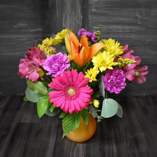 Bright mixed bouquet in an orange vase with pink, yellow, and orange flowers