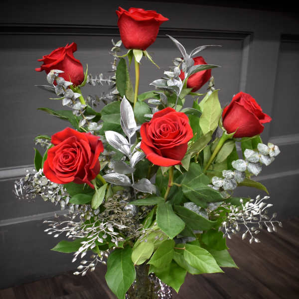 Red roses arranged in a clear glass vase with silver foliage