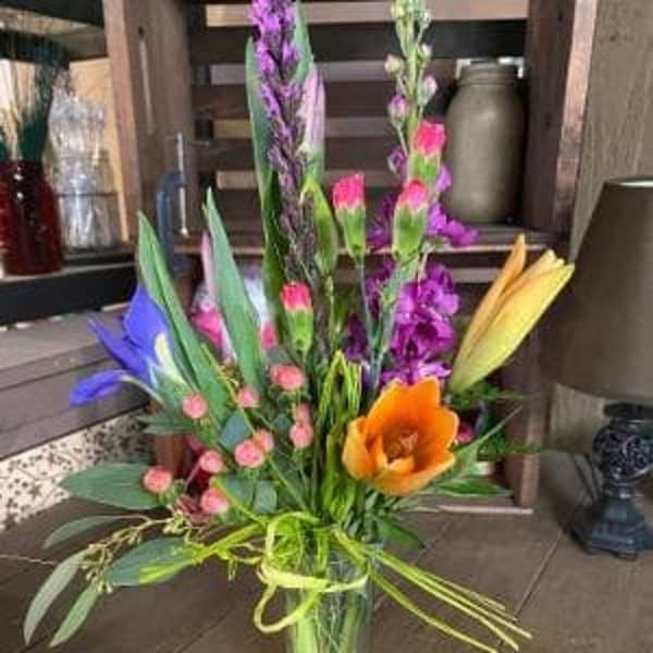 Tall mixed bouquet in a clear glass vase with orange, purple, pink, and yellow blooms