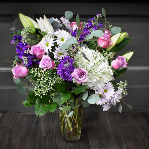Bouquet of pink roses, white lilies, and purple flowers in a glass vase