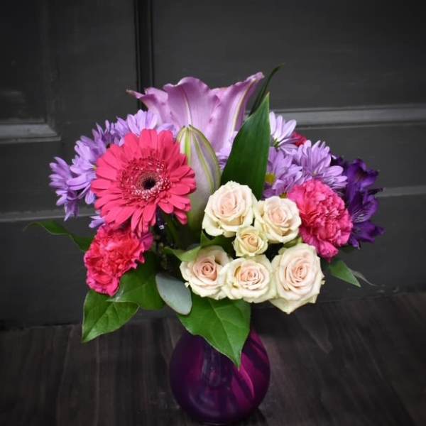Bouquet of pink, purple, and white flowers in a purple glass vase